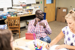Professional and Graduate student in a classroom, explaining something and gesturing while others take notes