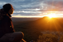 A student looking at the sunrise from atop a mountain