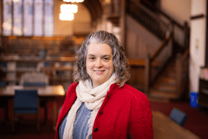 Alison West, a woman with short curly gray and black hair, wearing a red jacket, blue sweater and white scarf.