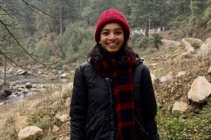 Supraja Balasubramanian (image description: a woman wearing a hat and a long jacket with trees behind her)