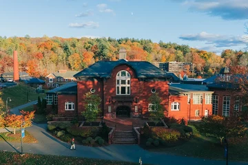 An aerial view of Mount Holyoke’s Blanchard Hall and Community Center in waning afternoon light, with colorful fall foliage and a blue sky in the background.