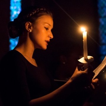 A singer uses candlelight to view music during a Vespers concert