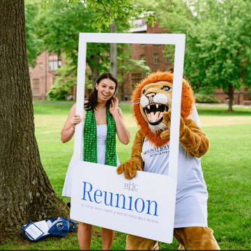Anl alum posing in a photo frame with Paws, the Mount Holyoke College mascot