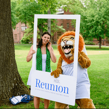 Anl alum posing in a photo frame with Paws, the Mount Holyoke College mascot