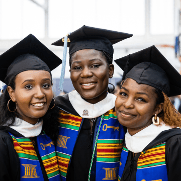 Three happy graduates in caps and gowns preparing for Commencement 2023