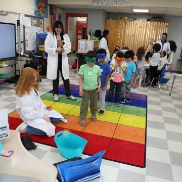 MHC students look on as first grade students try goggle brain activity.