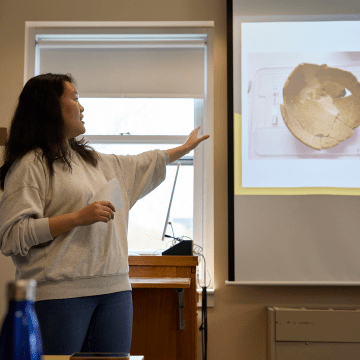 A student jestering at the projector screen while giving their presentation during Senior Symposium 2023