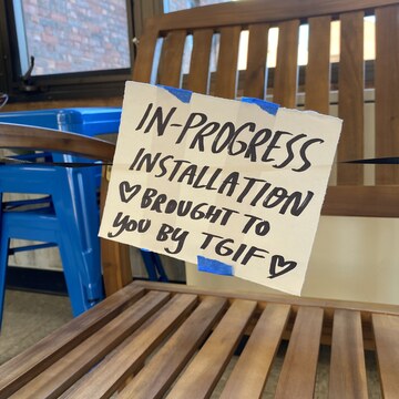 A sign on a chair in the Art Building Lobby "In Progress Installation brought to you by TGIF"