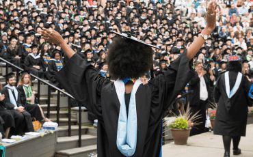 A student with arms raised after receiving their degree