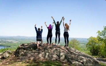 Four seniors cheering with arms raised at the top of Mount Holyoke