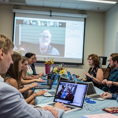 Professional and Graduate students in a classroom with a large screen for online students, showing an example of hybrid learning environment.