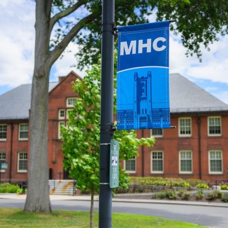 Mount Holyoke campus - a banner on a sign with MHC and the clock tower. Photo by Max Wilhelm, 2024.