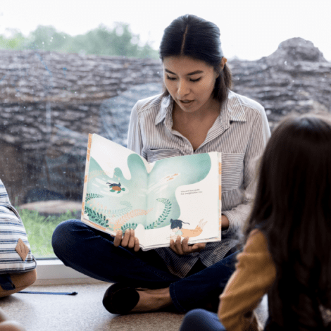 Woman reading book to students. Stock photo courtesy Canva.