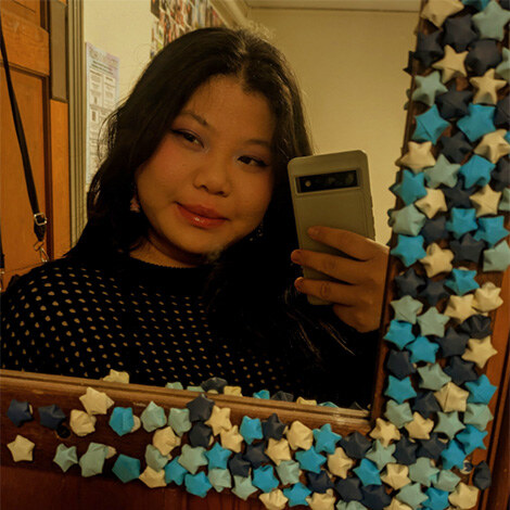 Miki Lin ’27 holds her phone up and takes a photo of their reflection in a mirror decorated with stars.