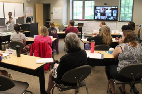 A graduate classroom, both in person and online with screens.