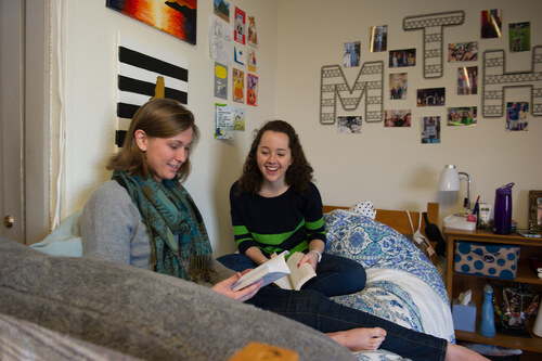 Two students sitting in a residence hall room reading books together
