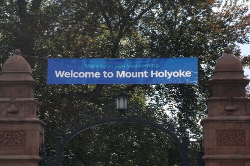 The front gate to MHC Campus with a blue banner that reads "Mary Lyon saw you coming. Welcome to Mount Holyoke".