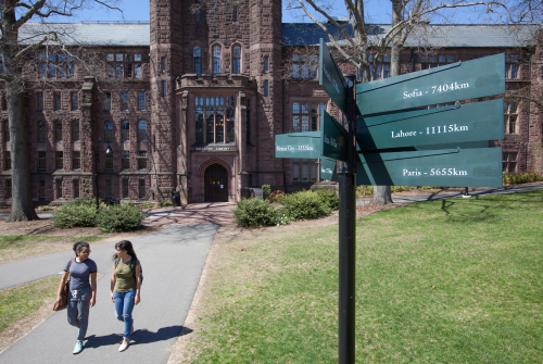 Aerial photo of two students walking near the library with the international signpost in the foreground