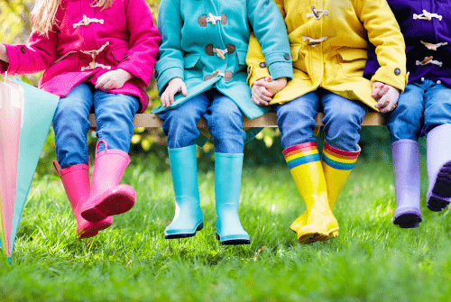 Children sitting on park bench wearing colorful rain boots