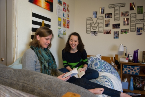 Two students sitting in a residence hall room reading books together