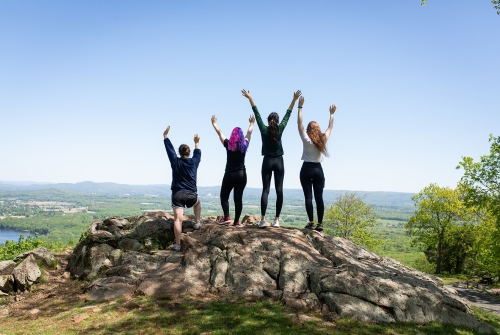 Four seniors cheering with arms raised at the top of Mount Holyoke