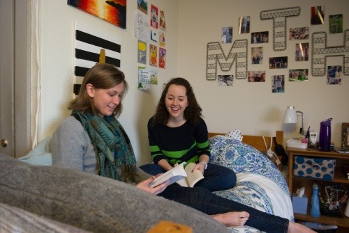 Two students sitting in a residence hall room reading books together