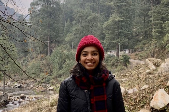 Supraja Balasubramanian (image description: a woman wearing a hat and a long jacket with trees behind her)