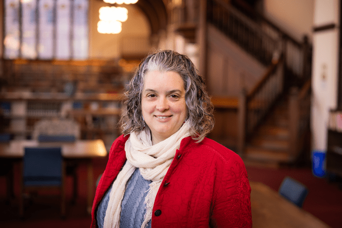 Alison West, a woman with short curly gray and black hair, wearing a red jacket, blue sweater and white scarf.