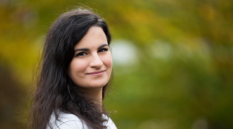 Katerina Drakoulaki, a woman with long dark brown hair, wearing a white shirt and smiling at the camera.