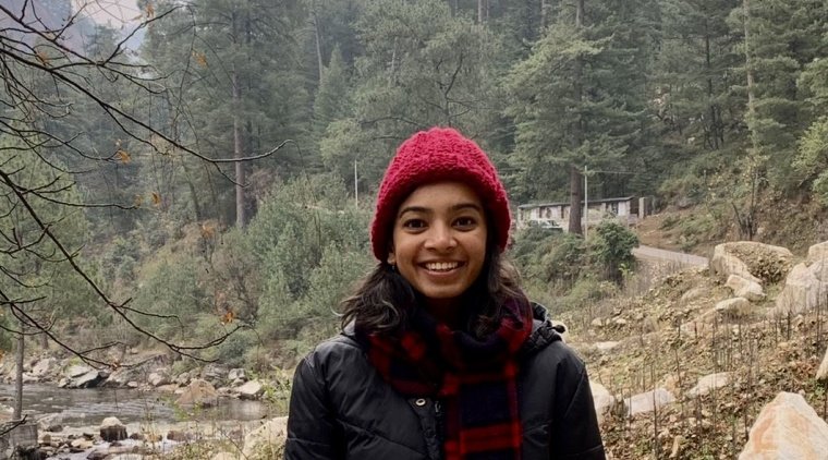 Supraja Balasubramanian (image description: a woman wearing a hat and a long jacket with trees behind her)
