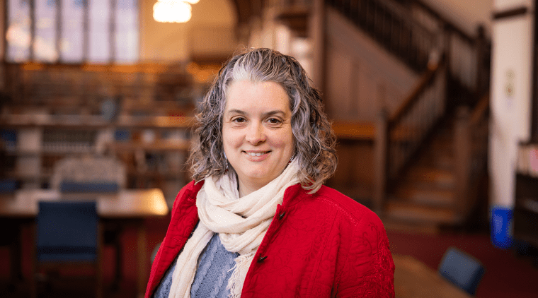 Alison West, a woman with short curly gray and black hair, wearing a red jacket, blue sweater and white scarf.