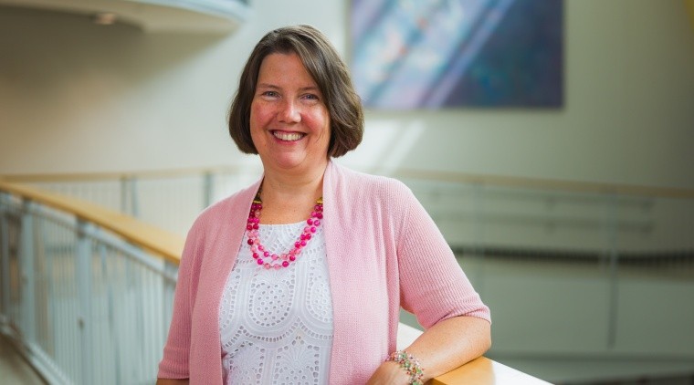 Dana Gillette, a woman wearing pink and smiling with brown hair.
