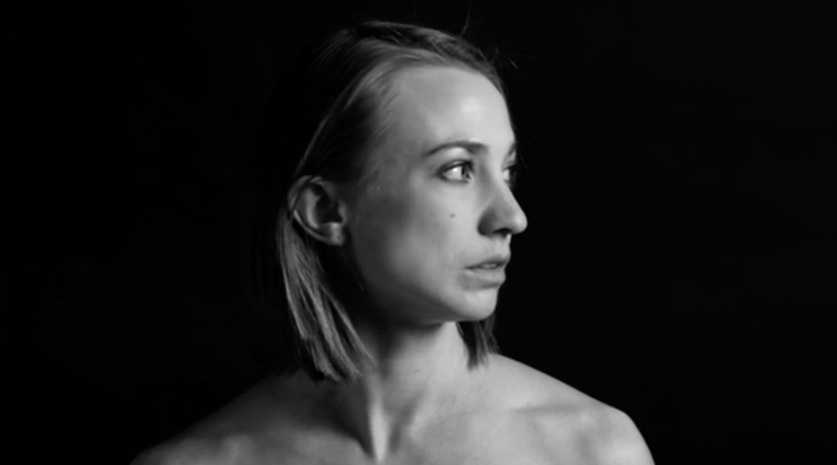 Ellie Goudie-Averill - a black and white photo of a woman with long hair looking to the right, a black background behind her, her face and shoulder lit by a light off screen.