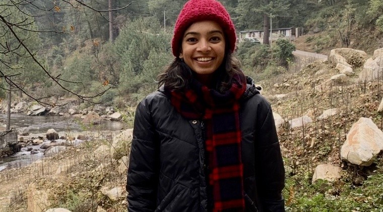 Supraja Balasubramanian (image description: a woman wearing a hat and a long jacket with trees behind her)