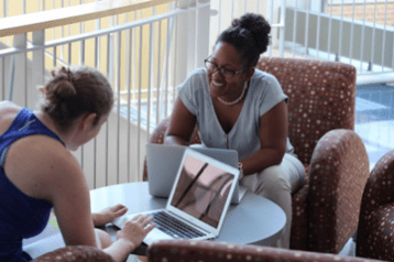 Two students in the graduate program discuss strategy while sitting together in Kendade.