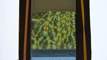 This image shows closely packed polyurethane disks placed between crossed polarizing filters, revealing forces that are usually invisible. The patterns of bright and dark lines can be used to find the contact forces between particles.