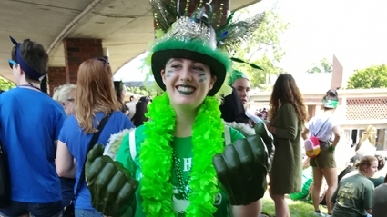 Junior Grace Alexander grins at the camera. She is decked out in a green top hat, lei, shirt and boxing gloves.