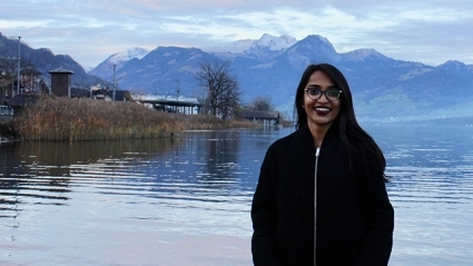 Woman with long black hair standing by a lake with snow-capped peaks behind her, near Geneva, Switzerland.