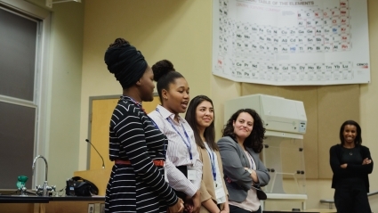 Four students, a panel at LEAP 2018, stand at the front of a lecture hall in Cleveland while a nearby professor listens.
