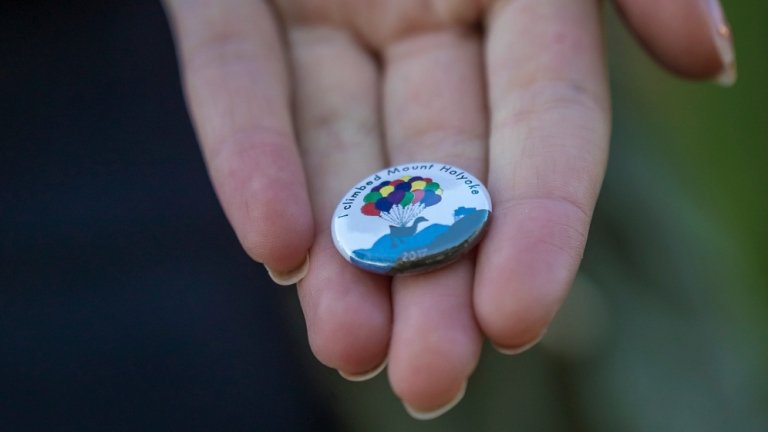 A hand holding an "I Clumbed Mount Holyoke" button.