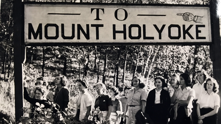 A group of students standing underneath a sign marking "To Mount Holyoke" on Montain Day 1946.