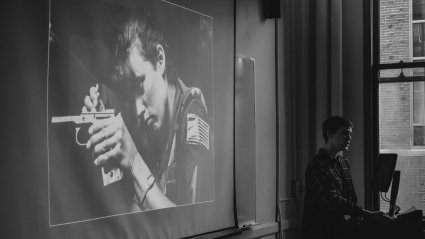 At LEAP 2018, a student speaks at a podium near a slide featuring a photo of a woman holding a handgun.