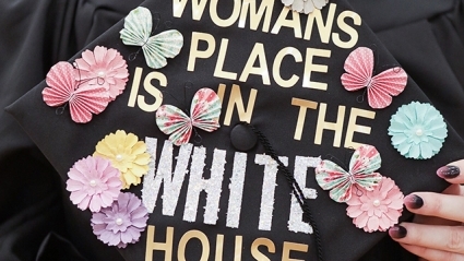 This is a close-up shot of a decorated mortarboard that reads, "A woman’s place is in the White House."