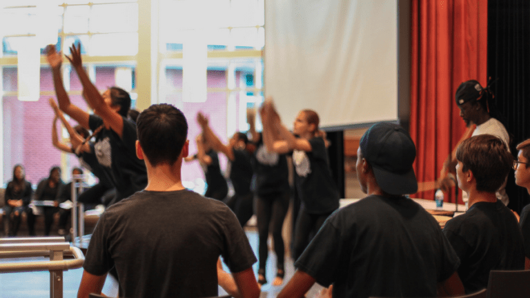 Student performance. Students with arms raised in the air as others look on.