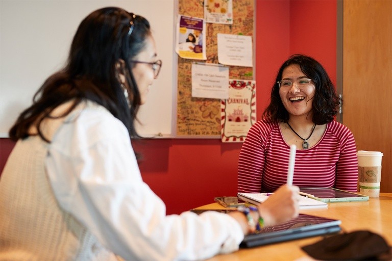 Two students  engaged in a discussion while seated at a table with tablets in front of them