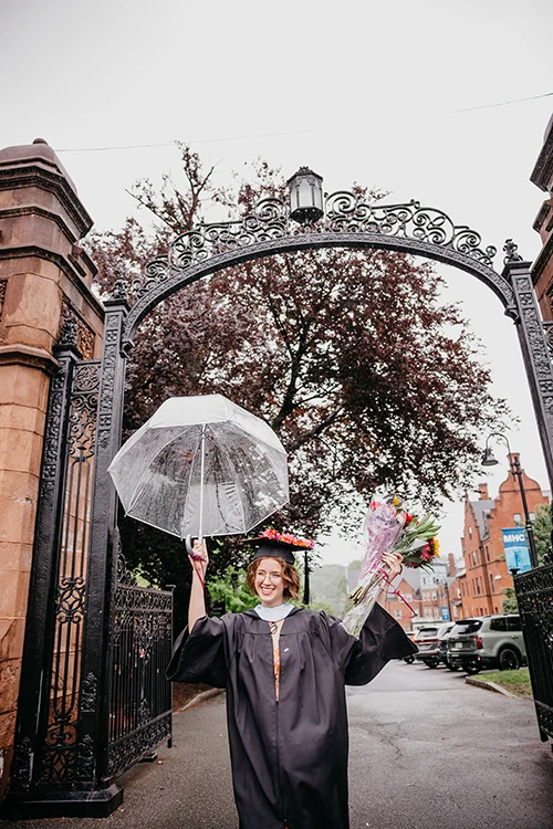MHC student holds up an umbrella in front of the gates after Commencement, 2026.