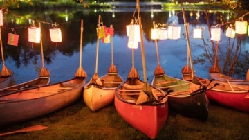 Canoes with lanterns lined up on the shore of the lake at twilight in advance of Canoe Sing.