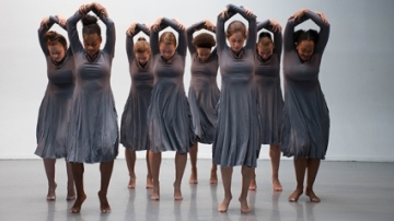 Eight dancers rehearse for "One," reaching up over their heads, bodies bent to the right.
