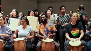 Michael Ofori, center right, and Faith Conant, right, drum with students as part of the final drumming, dancing and singing performance of their classes.