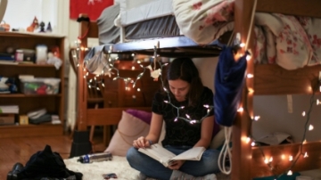 Student sitting on a bed reading a book in a Pearson's dorm room.